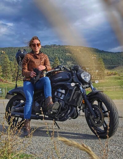 amber bahm sitting on black kawasaki vulcan motorcycle wearing a brown leather jacket with mountains in the background