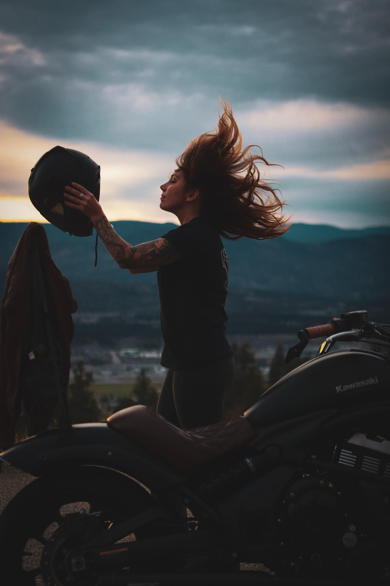 wild (1) woman throwing back hair while holding up motorcycle helmet standing near motorcycle