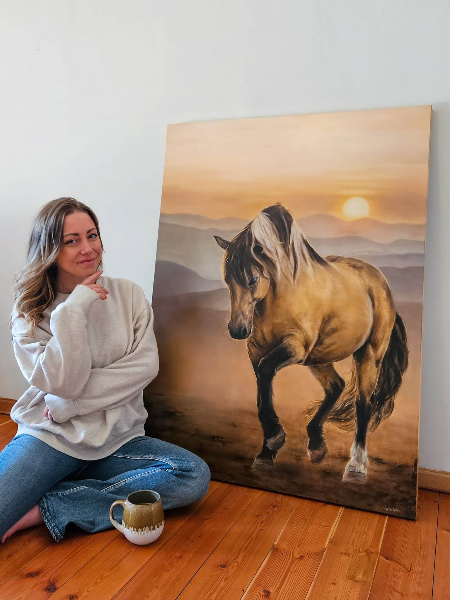 canadian fine artist amber bahm poses beside large painting of horse in front of sunset
