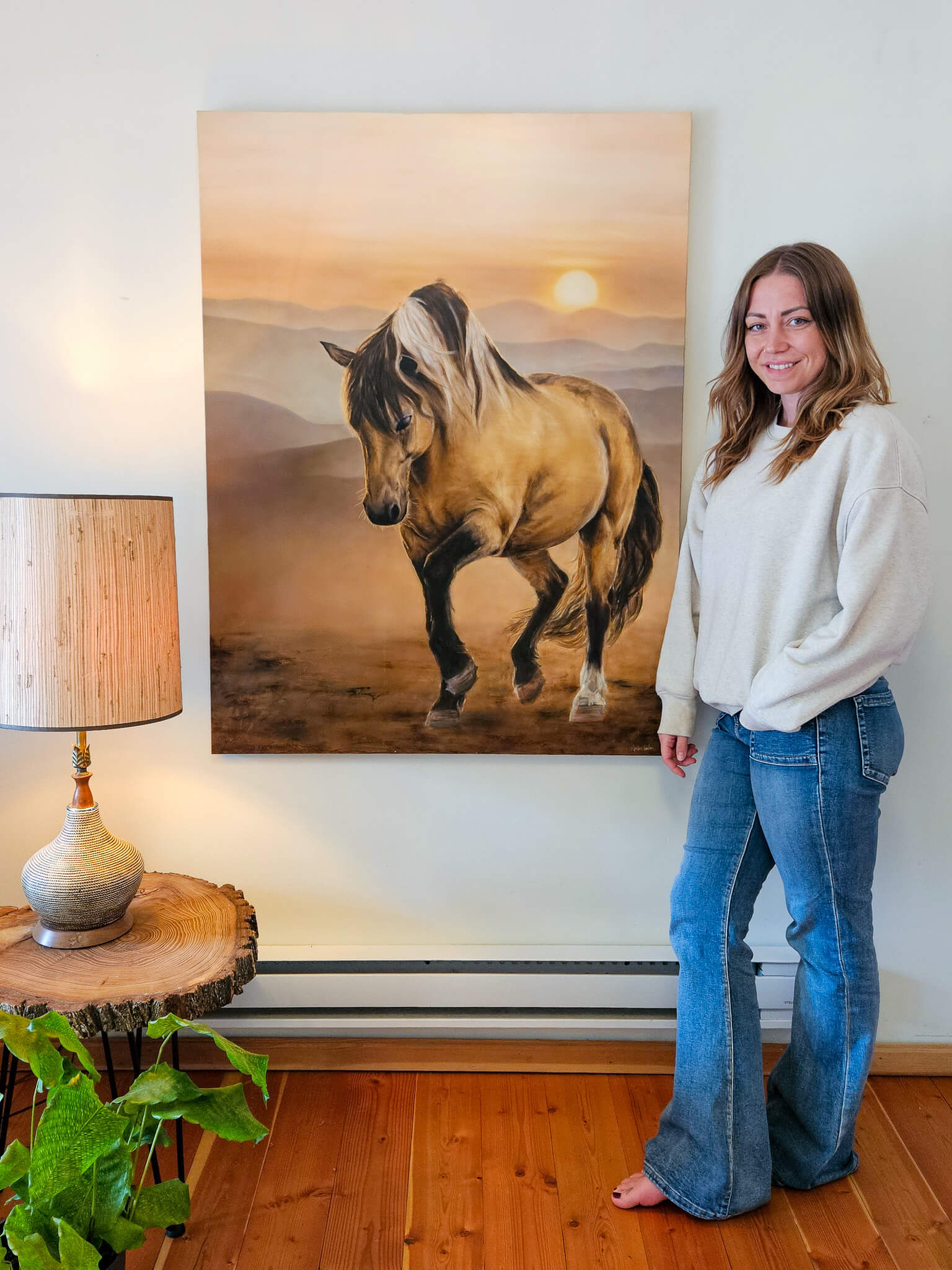 vancouver island based artist amber bahm stands beside beautiful large realism painting of a horse