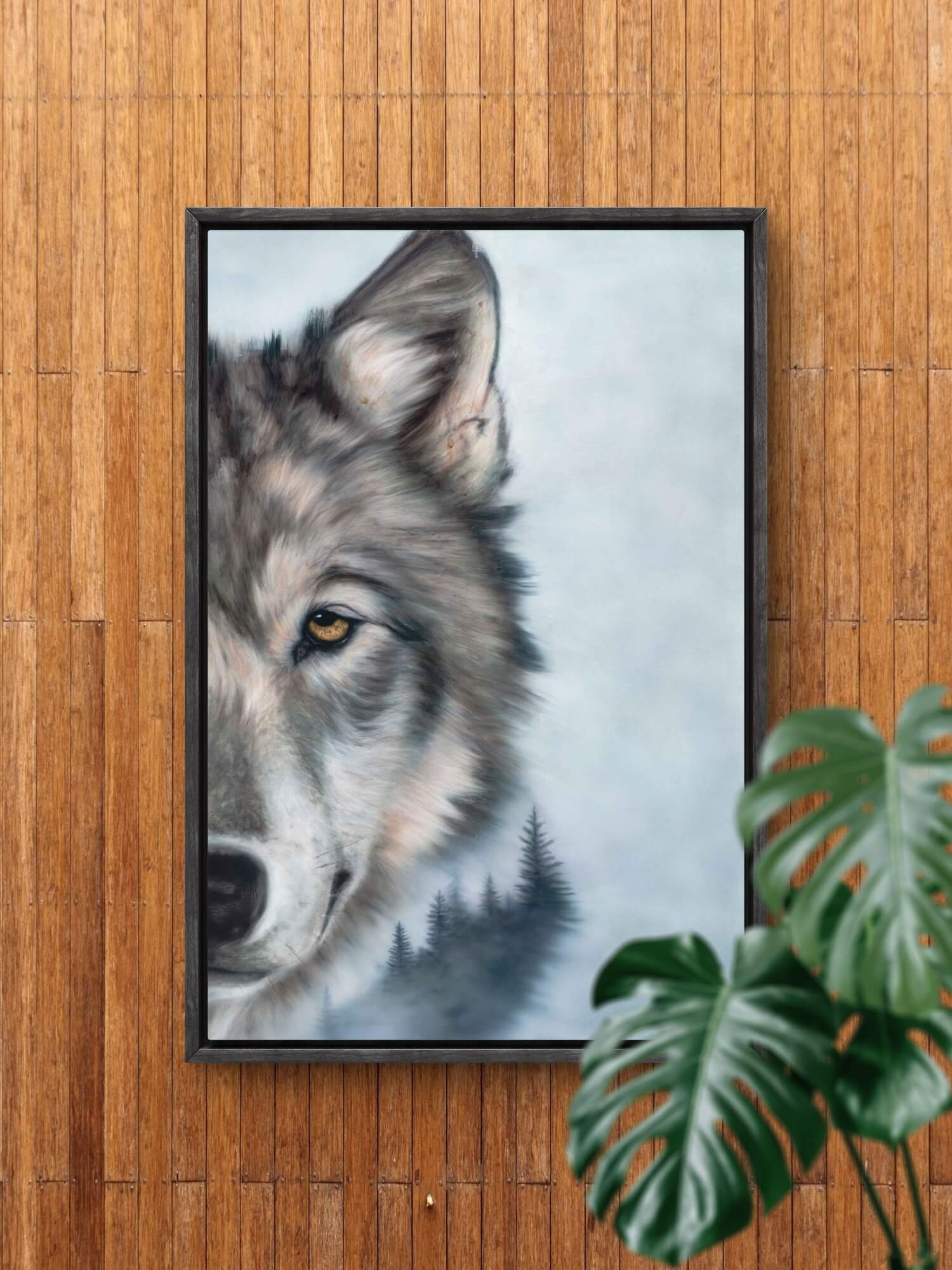 wolf and forest wall art in black wooden float frame on wood panel wall with monstera plant in foreground